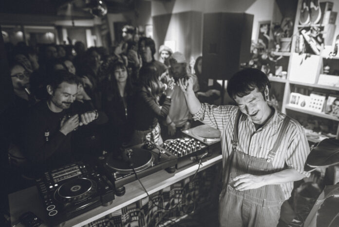 018 Tomoki Tamura DJing in a crowded record shop, black and white photo